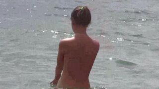 A group of naked beauties have fun on the beach, soaking up the sun